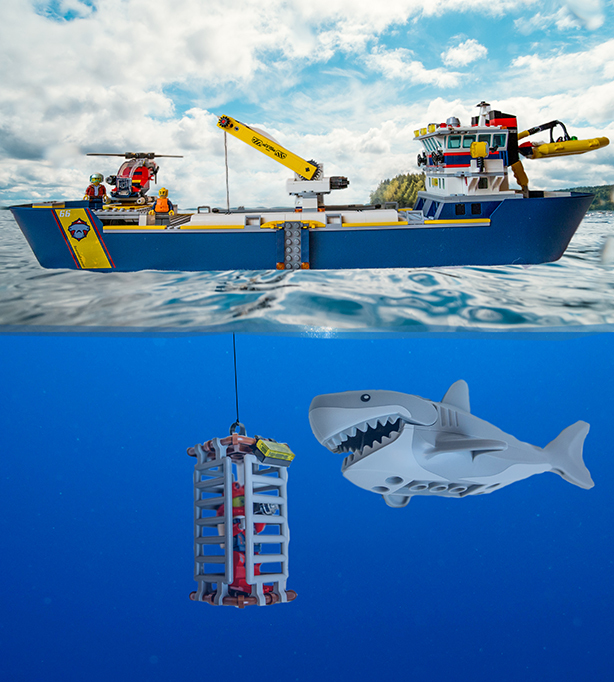 Legoista tehty asetelma, jossa sukeltajat häkissä pinnan alla kuvaavat haita. Pinnalla odottaa sukellustukialus.