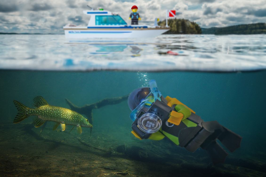 Legoista tehty sukelluskuvaaja kuvaa pinnan alla haukea, pinnalla odottaa sukellustukialus.